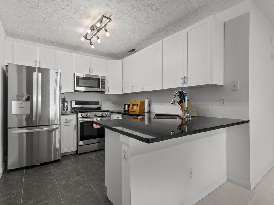 A kitchen with white cabinets, stainless steel appliances and dark countertops